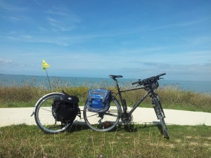 Vélo VTC aménagé pour le voyage avec roue-remorque de marque Extra Wheel, sacoches arrère et guidon (pas encore de sacoches avant) près du pont de l'Île de Ré (à proximité de La Rochelle) sur une piste cycblable croisant la Vélodyssée (EV1) sur le littoral atlantique