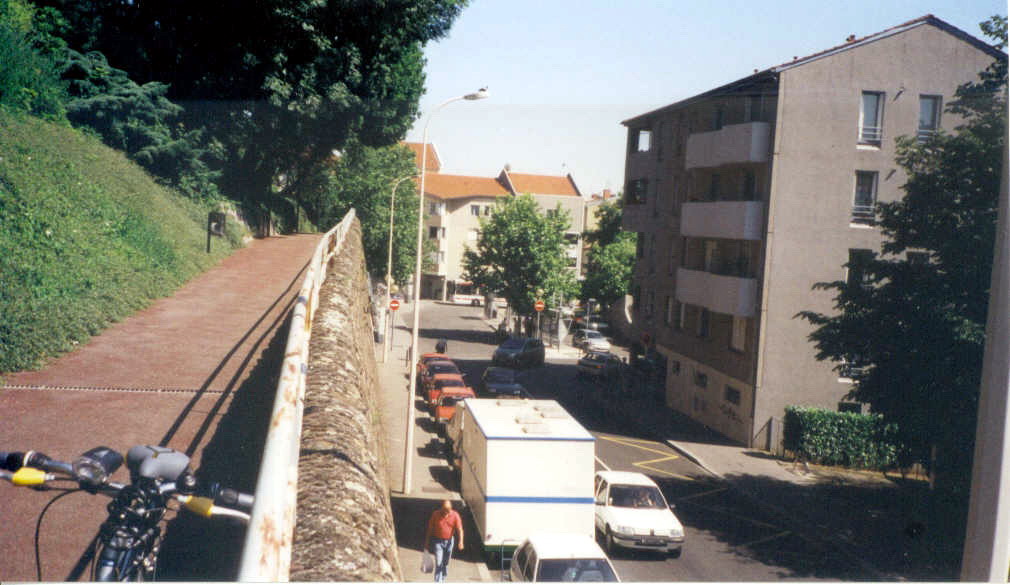 Nous sommes précisément sur le site de l’ancienne gare du FOL et le mur de soutènement à notre gauche est là pour nous le prouver. En face, nous avons la correspondance pour Saint-Jean qui se faisait déjà par le funiculaire (de 1872 à 1900) ou crémaillère (de 1901 jusqu'à 1957, la disparition du FOL ayant eu lieu en 1954) et de nouveau funiculaire depuis 1958. La découverte du FOL